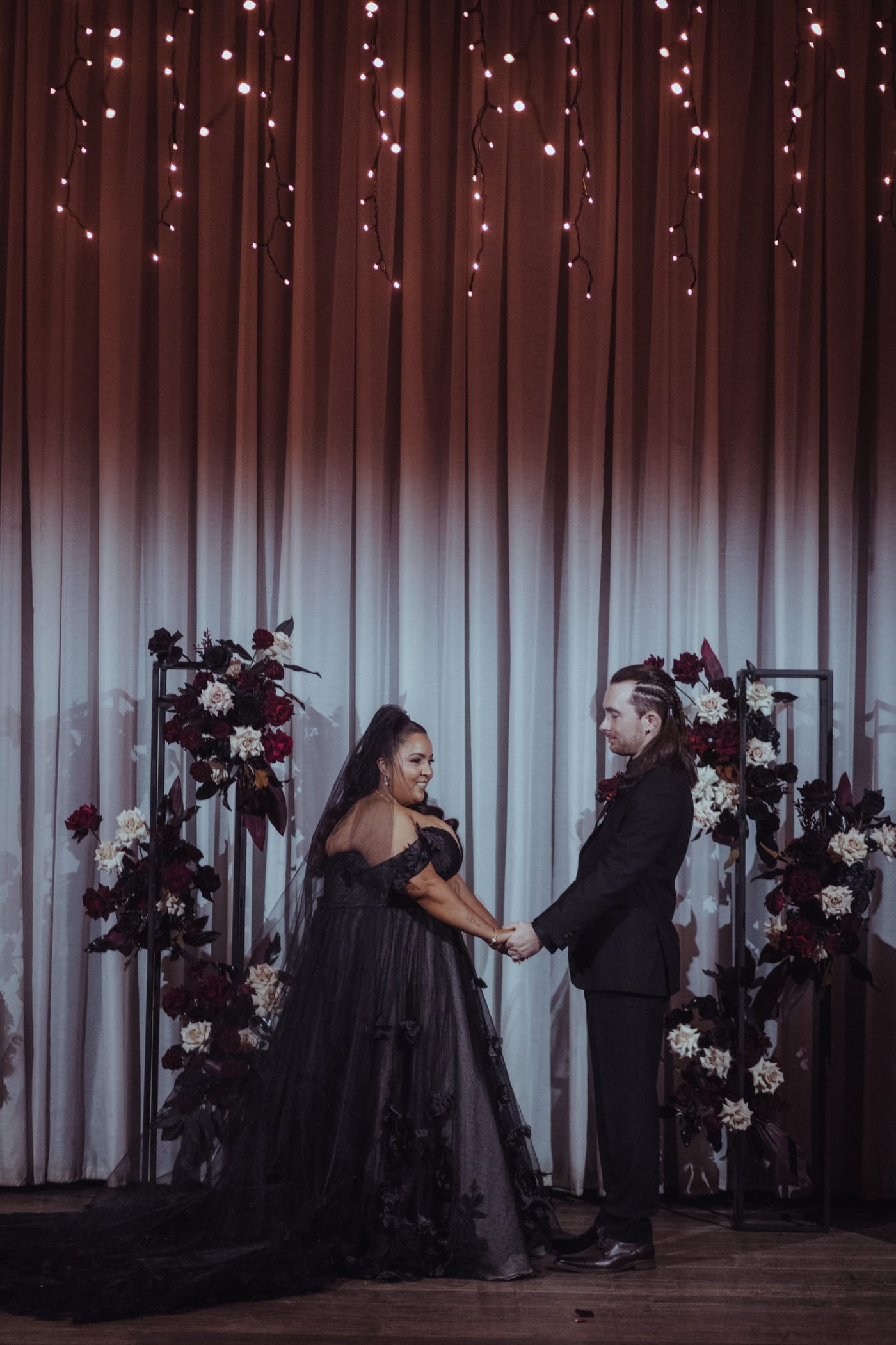 Couple at a dark floral wedding arch styled by Megan, Elder Emo Weddings